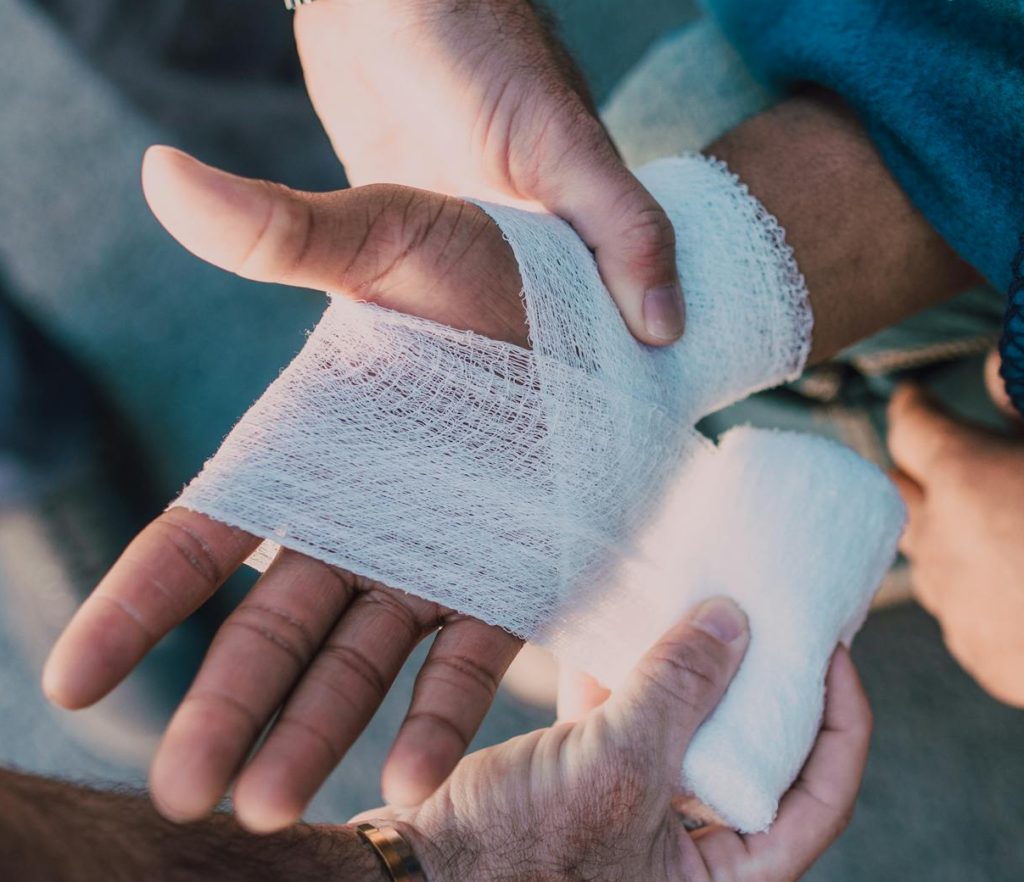Close-up of two people bandaging an injured hand outdoors, focusing on first aid care.